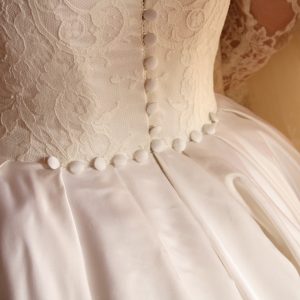 AMICIE - Robe corsetée en satin duchesse de soie et dentelle de calais. Traîne amovible boutonnée jusqu'à l'ourlet et manches en dentelle également boutonnées. Voile à l'ancienne en point d'esprit et dentelle de calais brodé à la main.